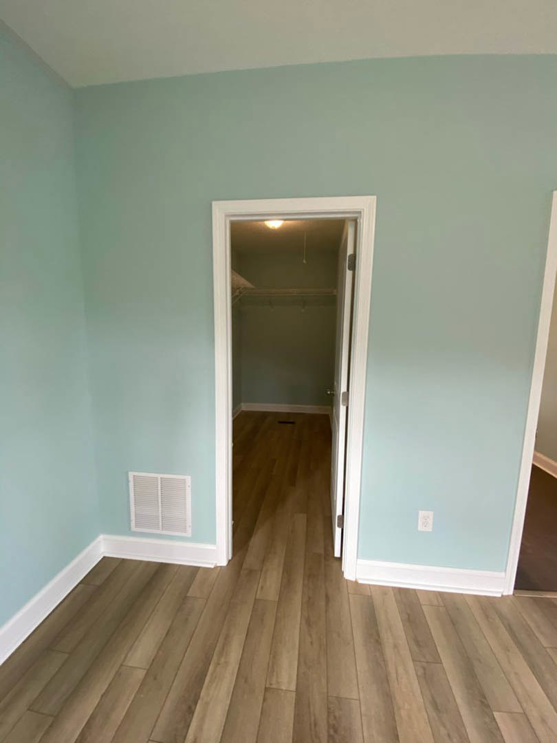Wood flooring in a room with white plaster walls, open door, and wall vent