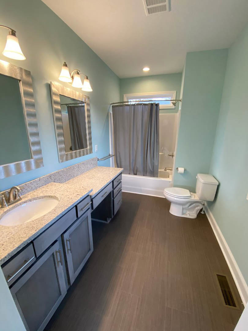 Modern bathroom featuring white tile walls, a rectangular sink with chrome faucet, wall-mounted mirror, white toilet, and dark wood cabinetry.