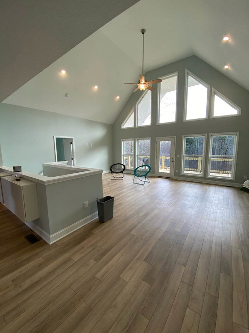 Open kitchen with wood flooring, ceiling fan, black framed chair, blue chair near window, black trash can, and reception desk against neutral walls