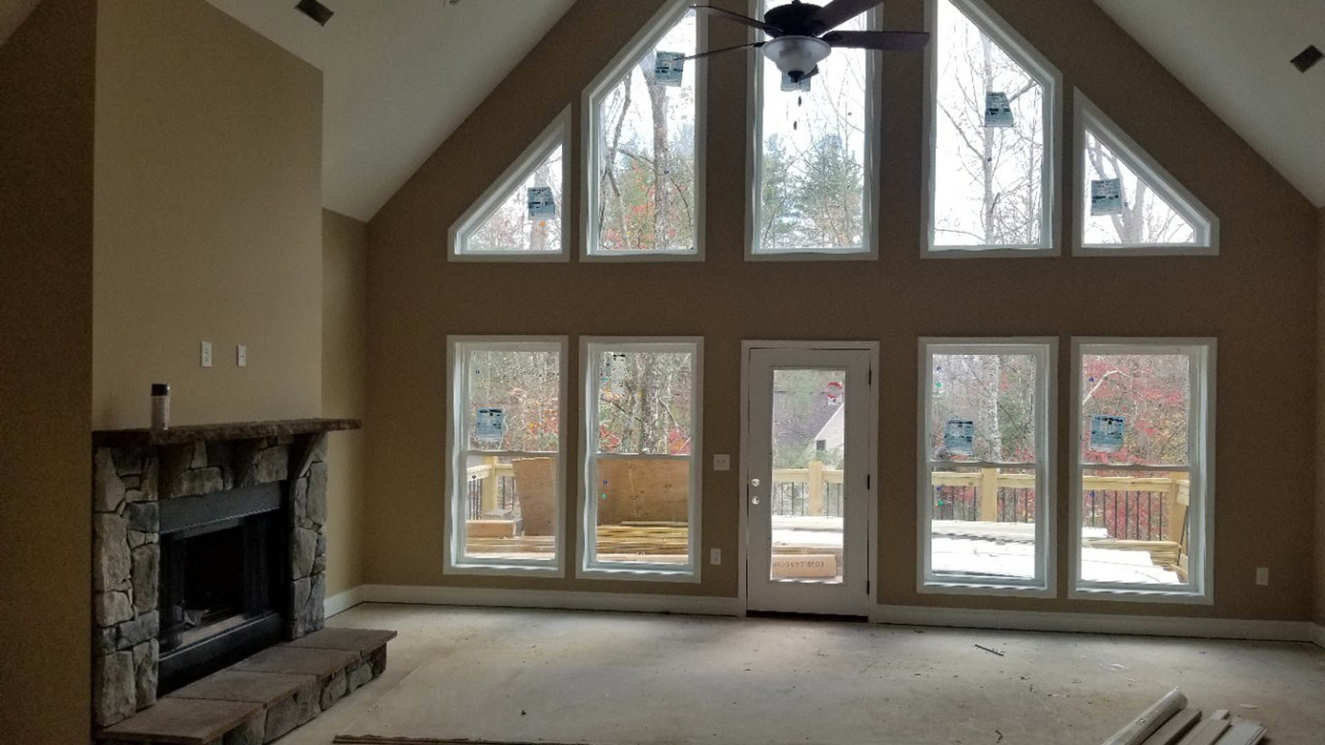 Living room with multiple tall windows, stone fireplace with raised hearth, ceiling fan, hardwood floors, and glass-paneled door