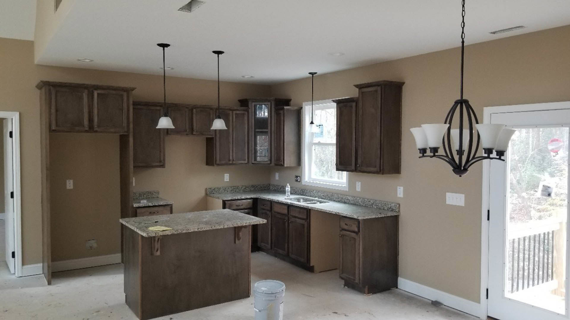 Granite countertops and wood cabinetry in a kitchen, stainless steel sink with chrome faucet, marble-topped counter, white wall outlet with black buttons, window with paper taped