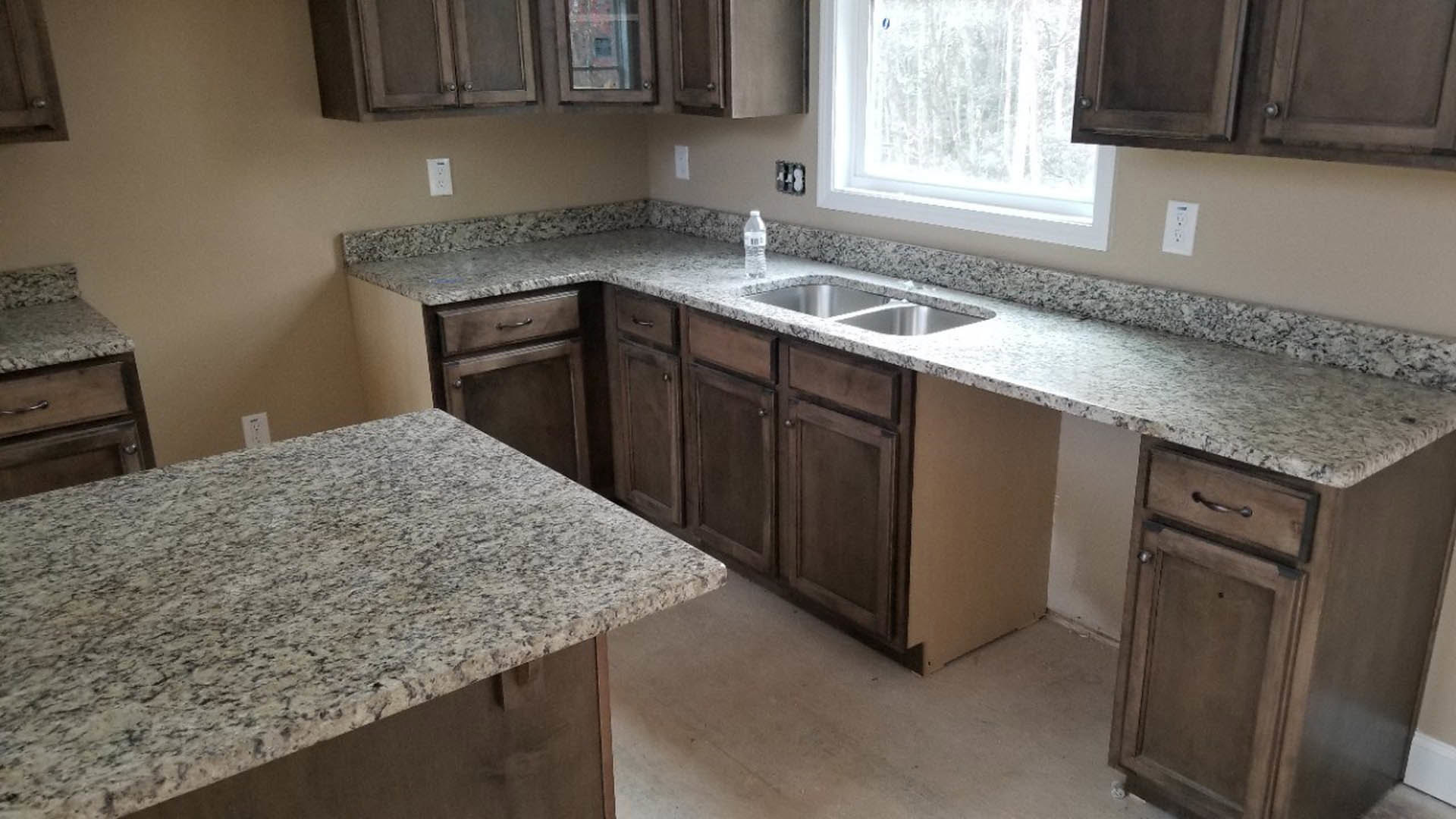 Granite countertops with white and brown walls, stainless steel sink, tile backsplash, cabinetry, window overlooking outdoors, white electrical outlet and appliance with black