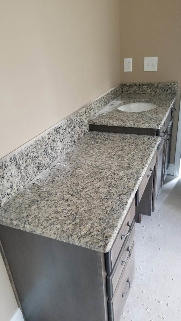 Granite kitchen countertop with stainless steel sink, white cabinetry, drawers, and dual light switch on tiled wall