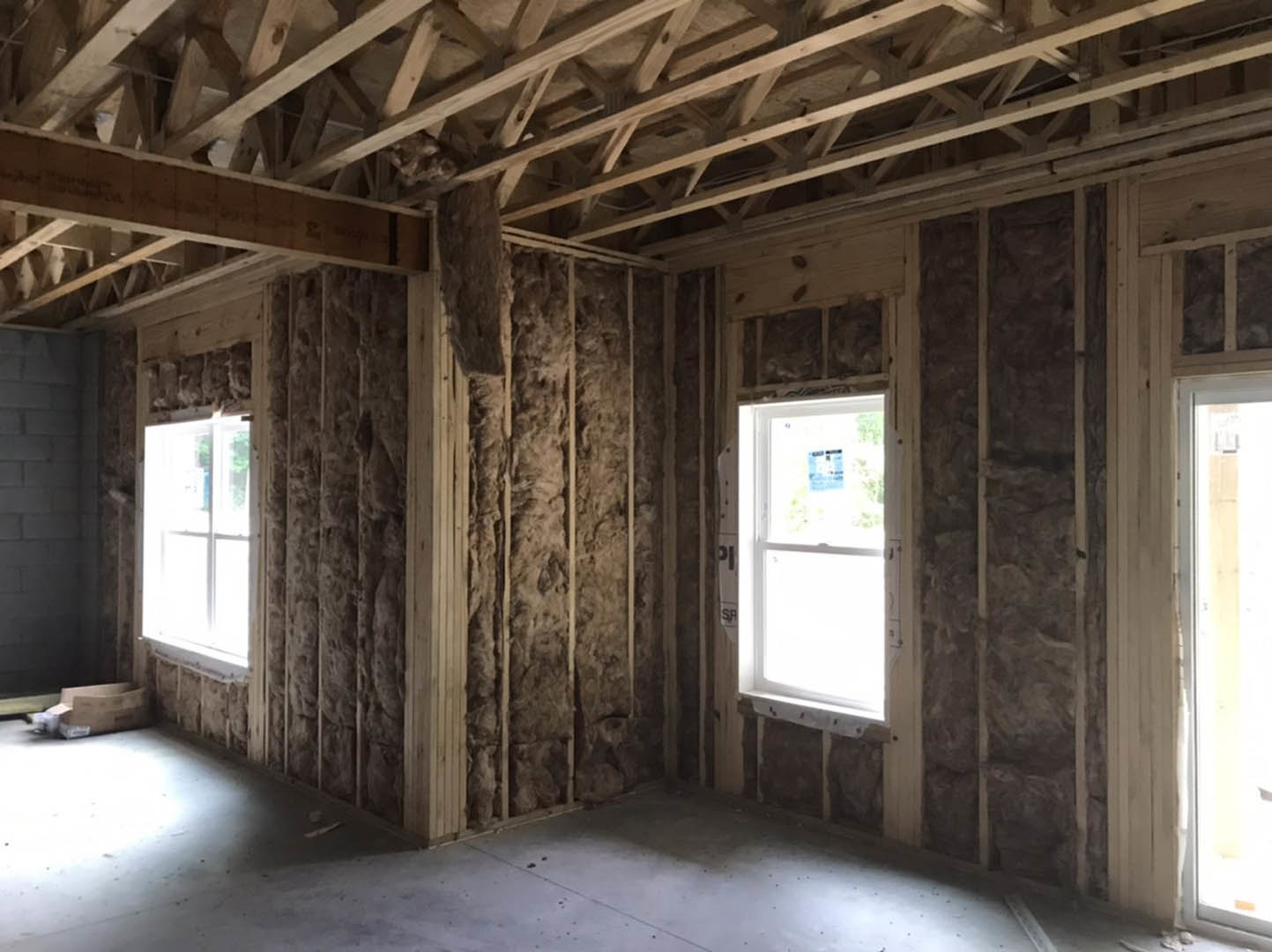 Exposed wood framing and ceiling beams, large windows with natural light, brick accent wall, construction sign visible on window glass
