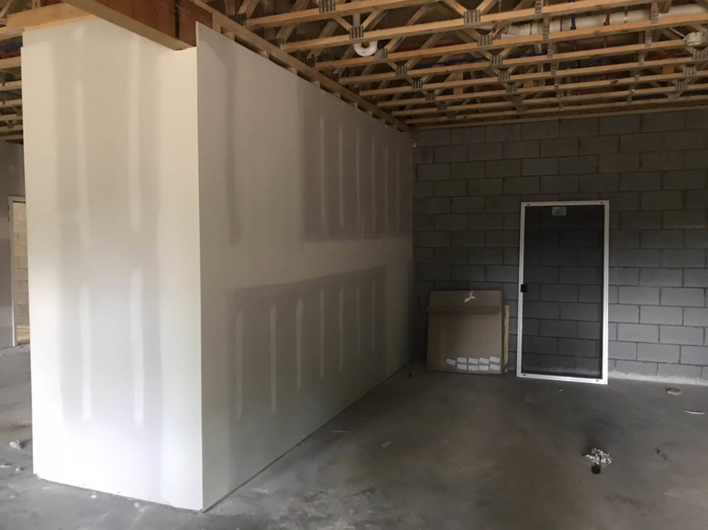 Exposed brick accent wall with wooden ceiling beams, white plaster walls, concrete floor, and a single door set into the brick wall