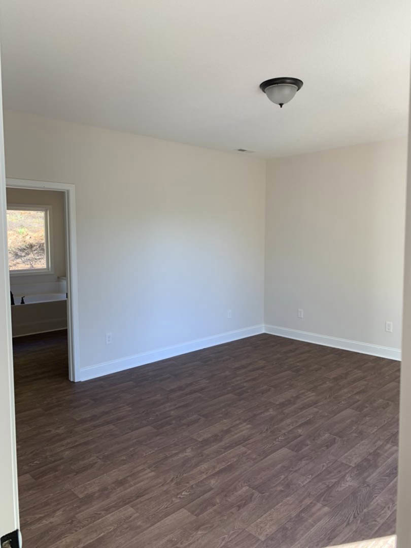 Open living space with wide plank wood flooring, white plaster walls, and a modern pendant light fixture hanging from the ceiling