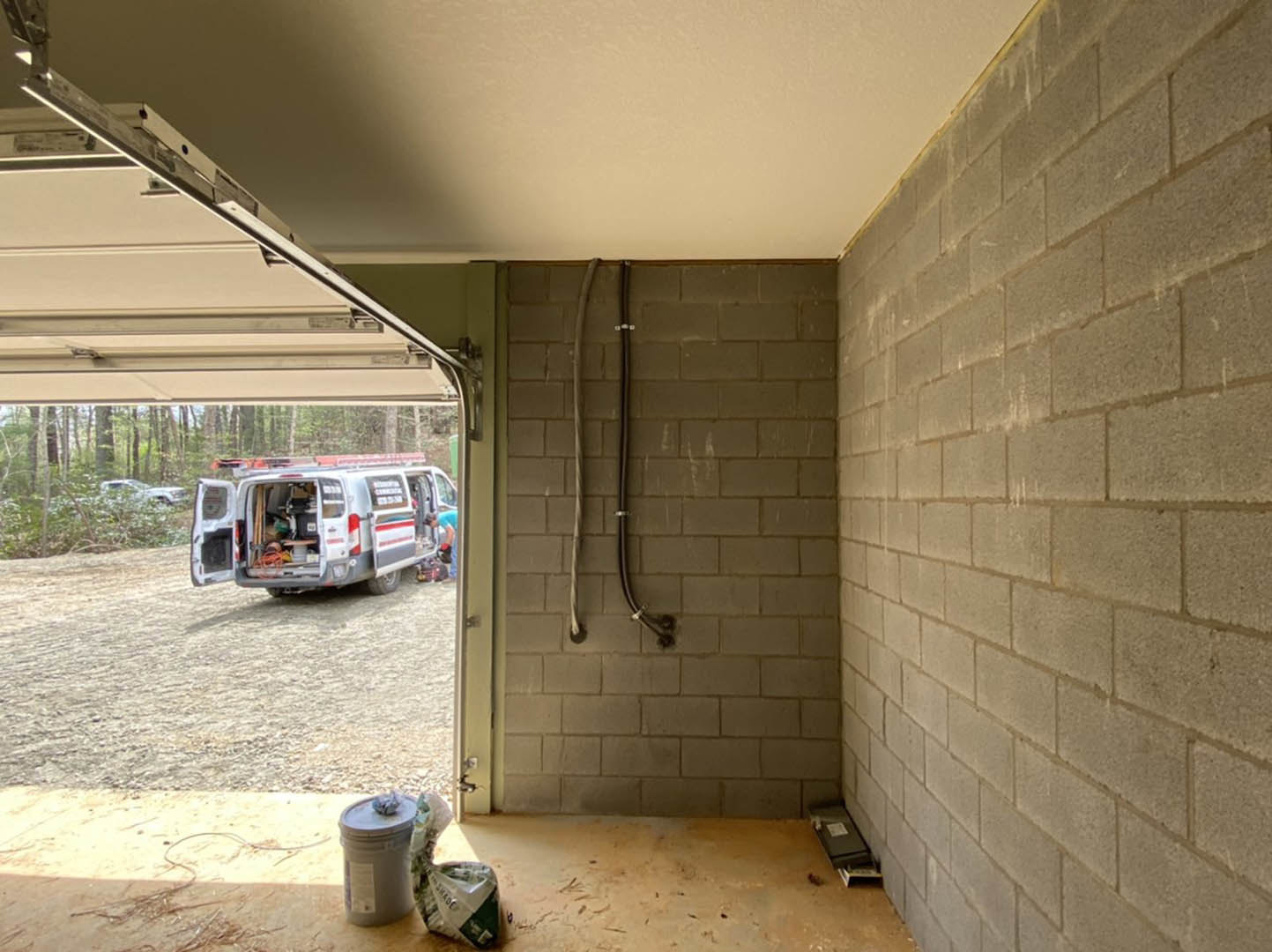 Open garage with concrete floor, white waste container, visible van parked inside, building wall and exposed ceiling structure