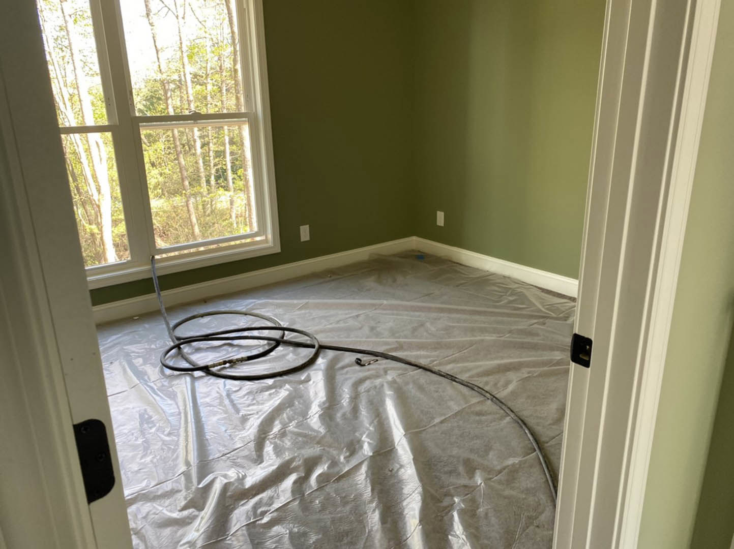 Black hose lying on white plastic-covered floor in unfinished room with window showing trees outside