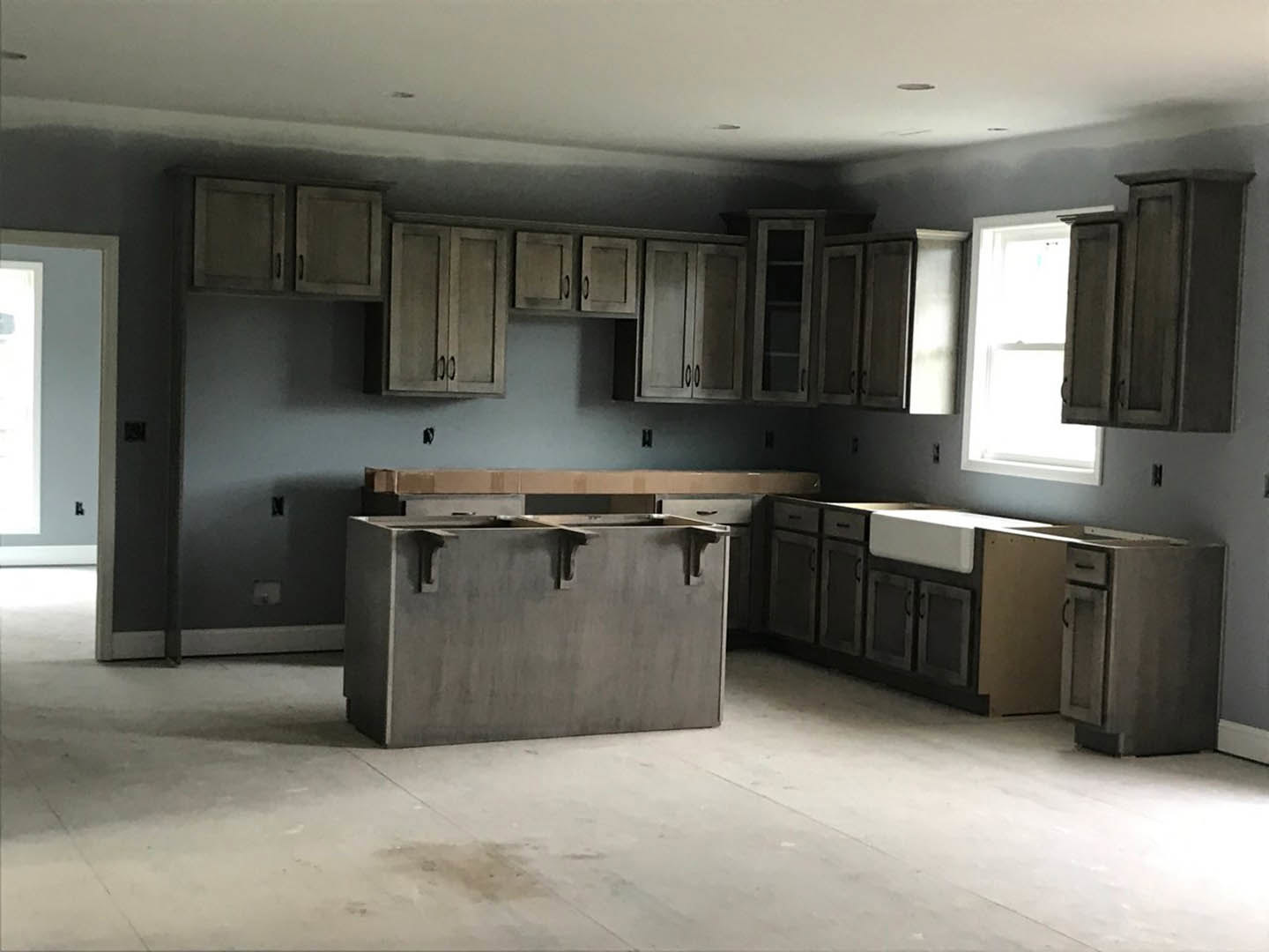 Modern kitchen featuring white shaker cabinets, quartz countertops, stainless steel sink, large window with natural light, light grey walls, and dark hardwood flooring
