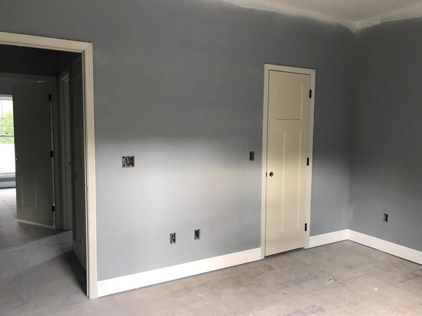 White interior room featuring two paneled doors, smooth plaster walls, light wood flooring, and a simple ceiling.