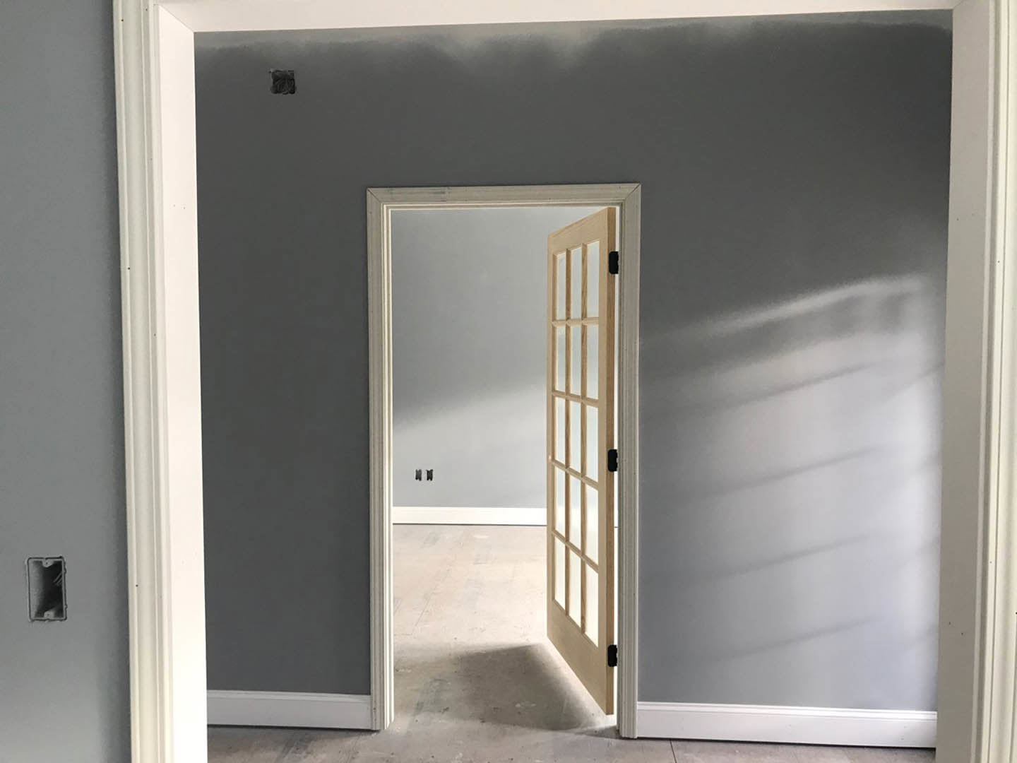 White painted door with brushed metal handle set in a smooth plaster wall, hardwood floor visible, soft shadow cast along baseboard.