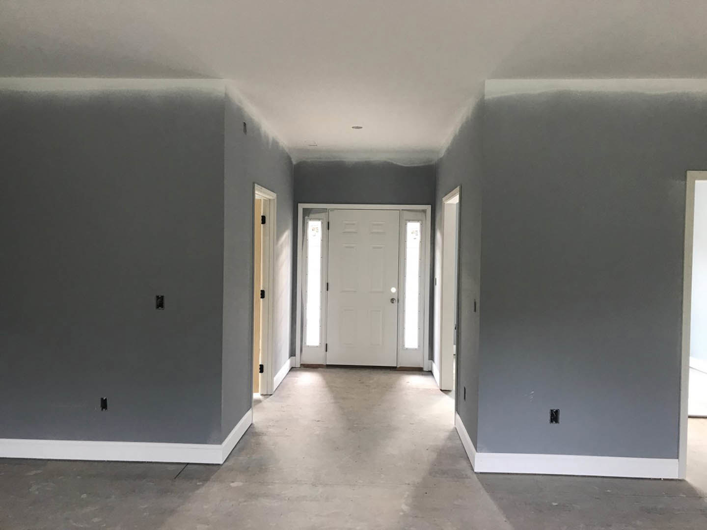 Hallway with gray walls, white doors featuring glass panes, recessed ceiling light illuminating light-colored flooring, visible wall-mounted light switch