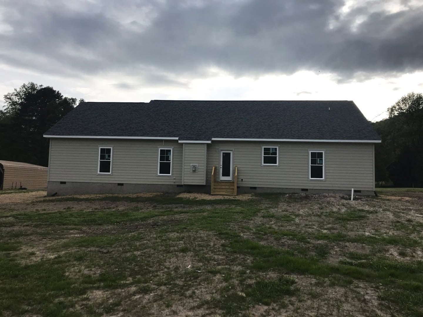 Two-story cottage-style home with white siding, black-trimmed windows, wooden front door, covered porch, manicured lawn, and overcast sky.