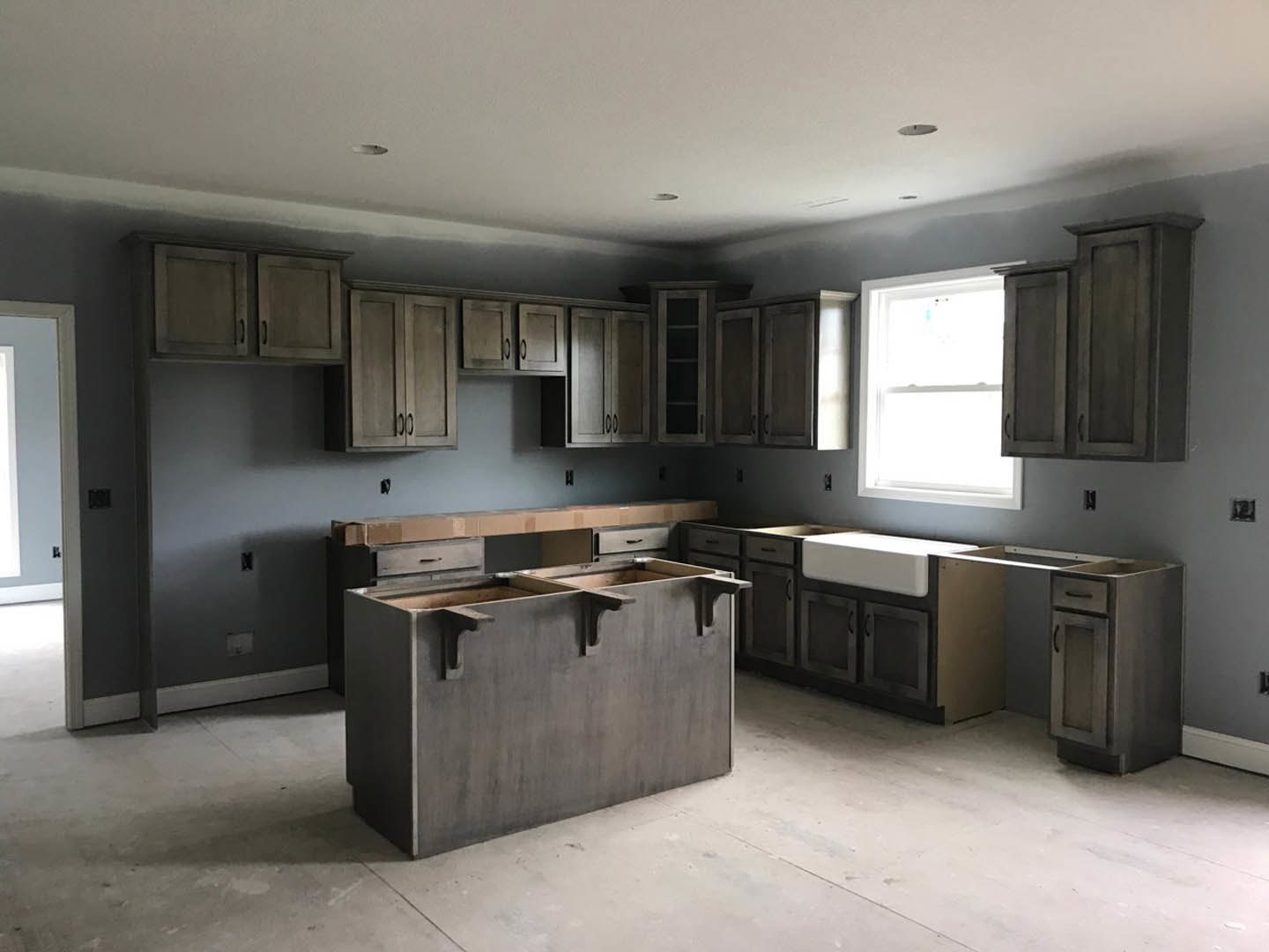 Modern kitchen with white cabinets, stainless steel sink, grey drawers, light stone countertop, large window with white frame, and neutral grey walls