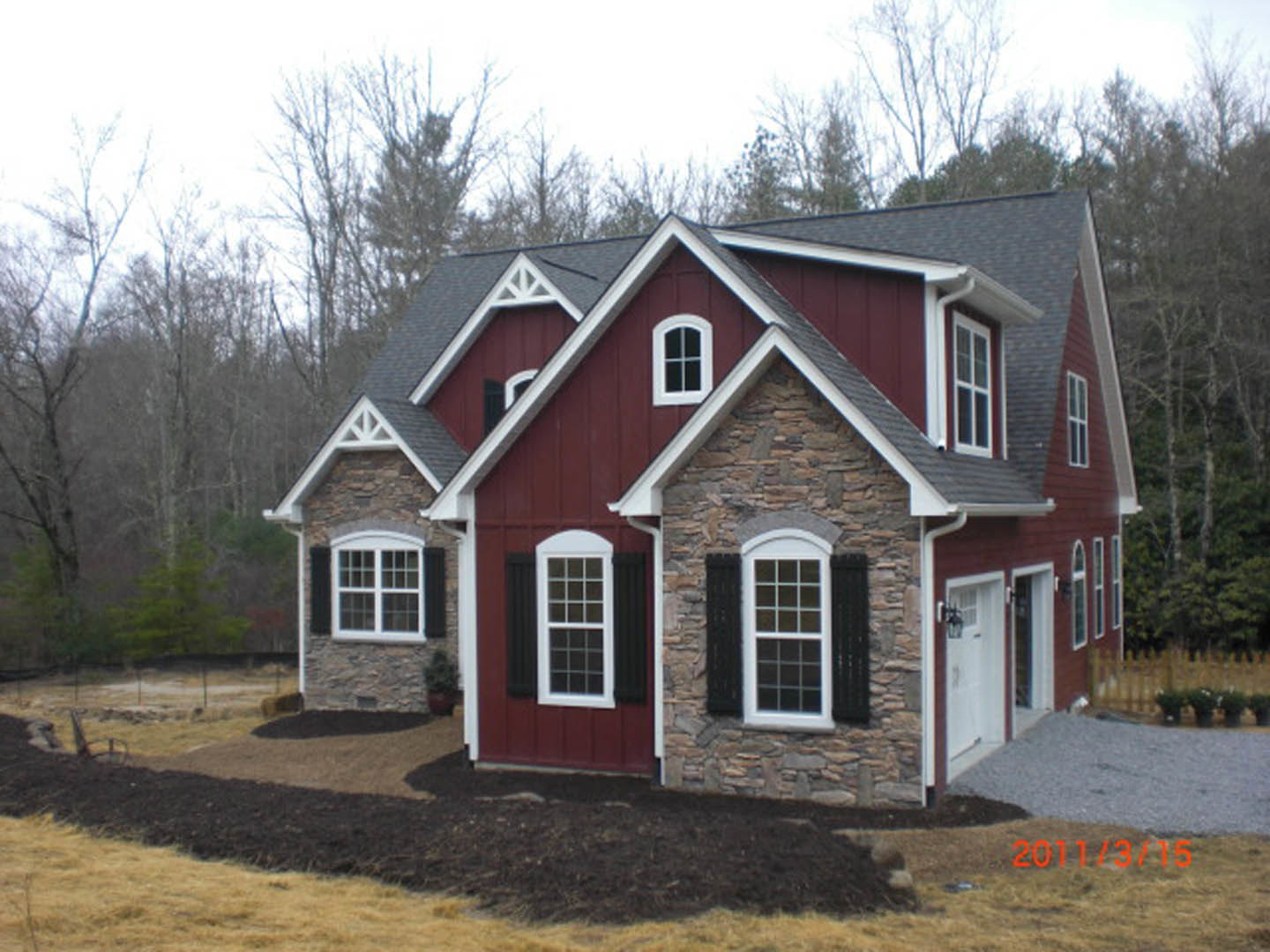 Red and white exterior with stone and brick accents, white-trimmed window, white door, grey gravel surface, and dirt patch in front yard