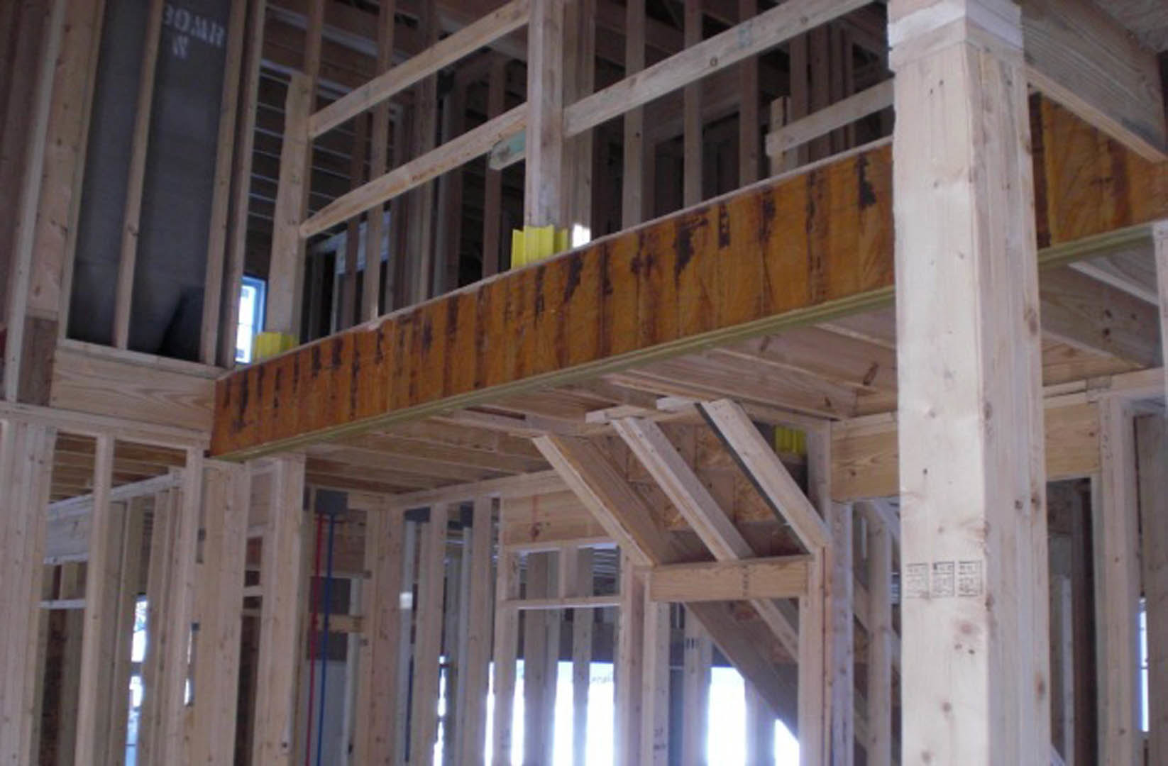 Exposed wooden ceiling beam with yellow paint, surrounded by unfinished framing and insulation in a residential interior