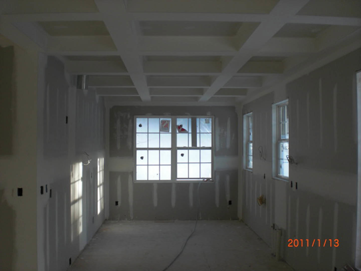 Bright room featuring multiple large windows, white ceiling beams, plaster walls, and light wood flooring