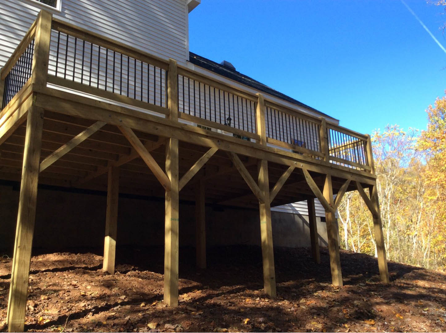 Wood deck with metal railing attached to house, surrounded by autumn trees with yellow leaves, log cabin siding, and blurred fall foliage in background