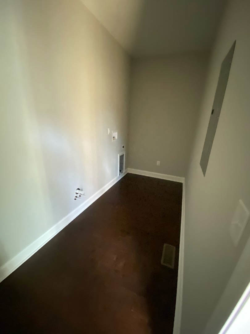 Hallway with dark wood flooring, white plaster walls, a floor vent, and electrical outlets visible along the baseboard