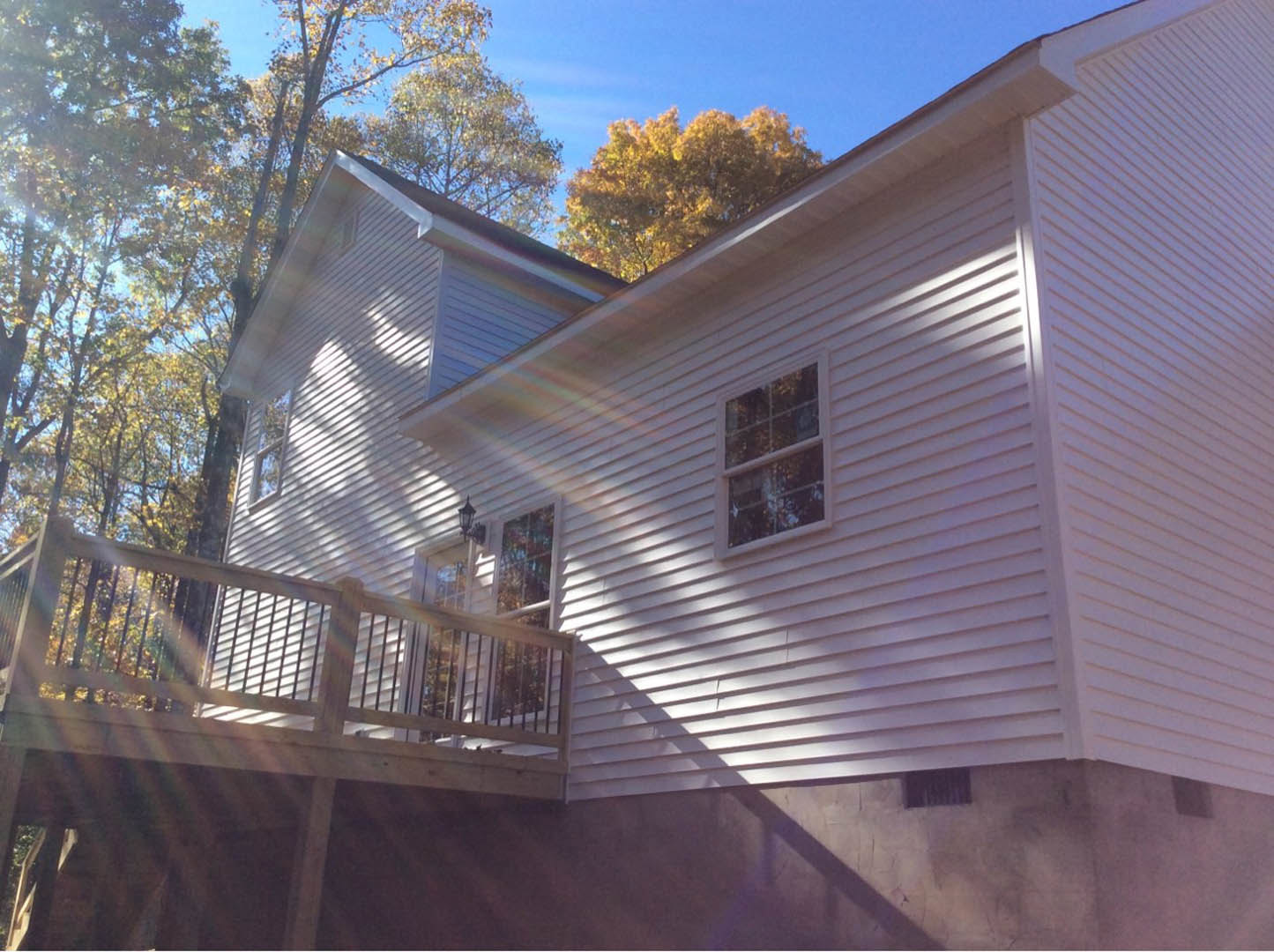 Modern home with light siding, large windows, and wooden deck surrounded by mature trees with yellow foliage
