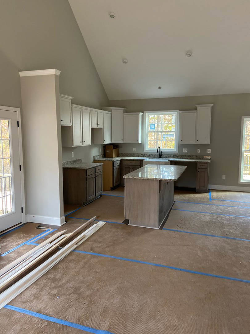 Kitchen with marble island countertop, wood plank flooring, white cabinetry, window above sink with black faucet, and white door with black handle.