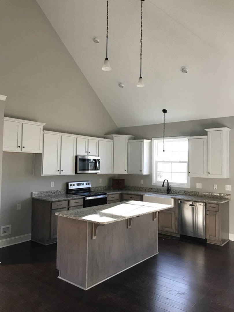 Spacious kitchen featuring a large granite island, stainless steel appliances including microwave and refrigerator, white cabinetry, stove with drawers, pendant light fixture above