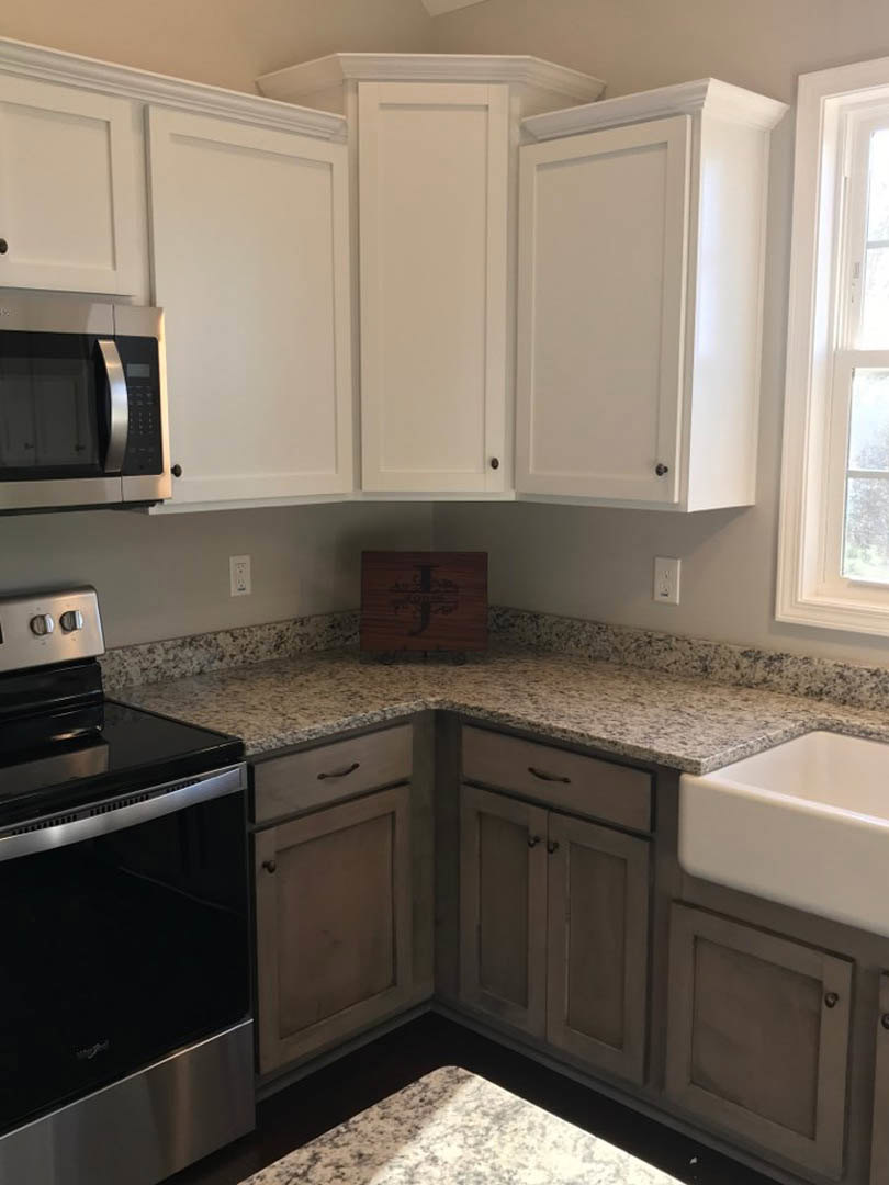 White kitchen cabinets with granite countertops, stainless steel oven and microwave, close-up of sink, wooden box with letter J, white door frame with window.