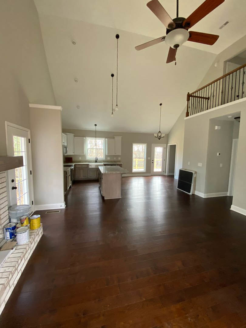 Spacious open-concept living area featuring laminate flooring, central fireplace with white surround, ceiling fan with light, adjacent kitchen with large island, and visible