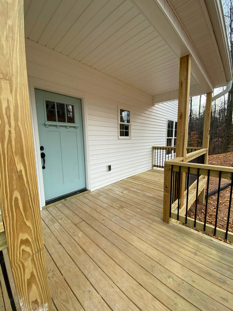 White siding house with blue front door, wooden deck and railing, white framed window, and front porch stairs