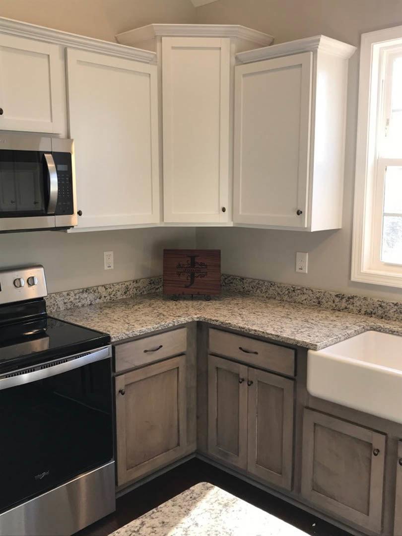 White shaker cabinets, black freestanding stove, granite countertops, stainless steel sink, built-in microwave, window with key in lock
