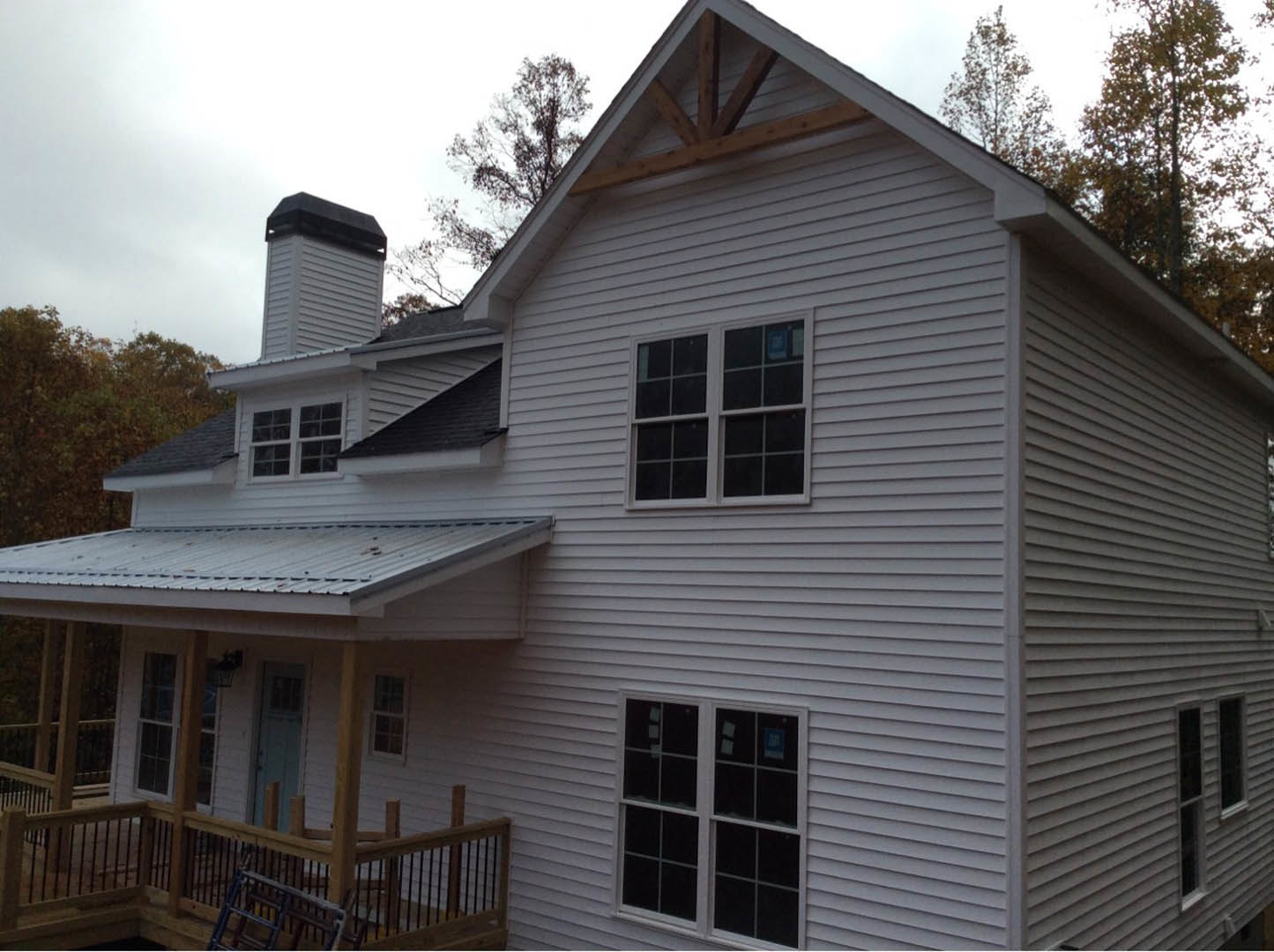 Front porch with wood railing, white siding, metal roof, large window, blue ladder leaning against fence, leafy tree in foreground
