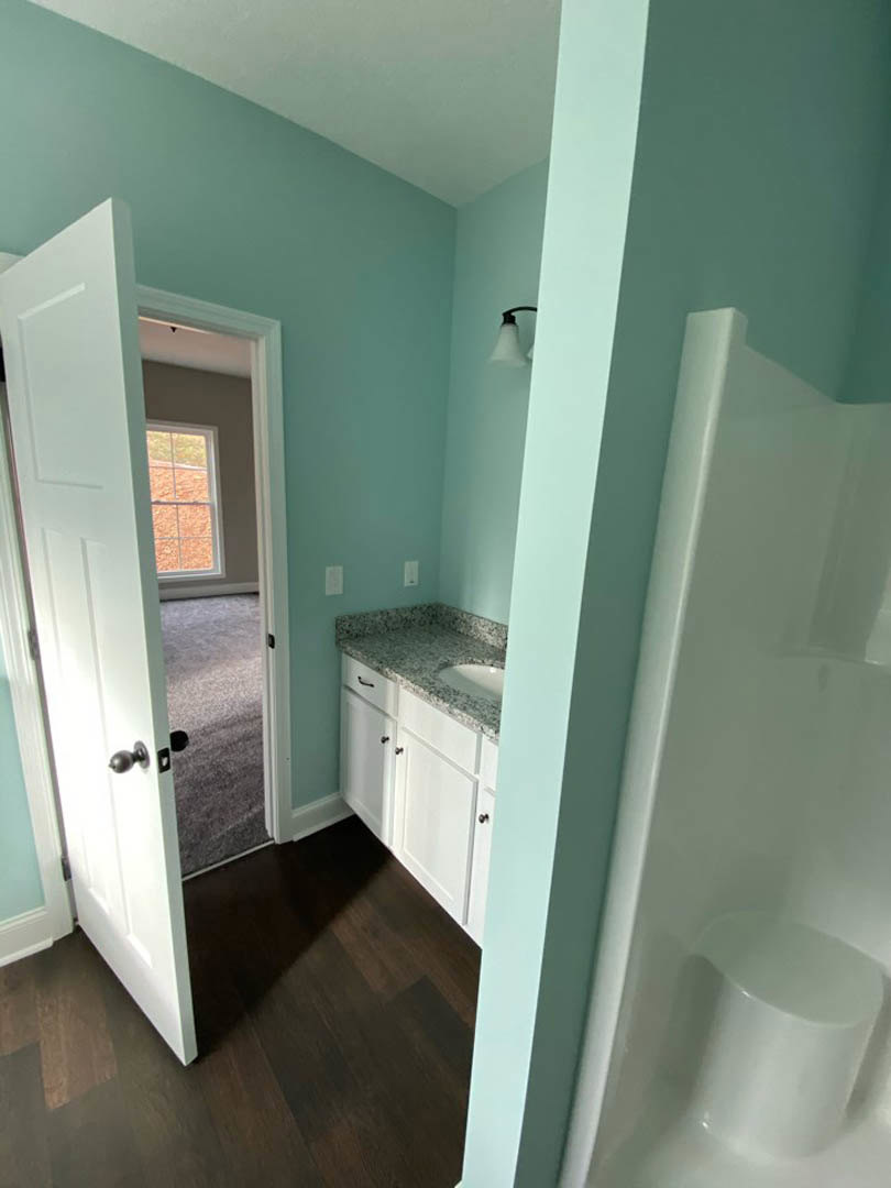 Bathroom featuring a white sink and chrome faucet, glass-enclosed shower with tile walls, white-framed window, dark wood flooring, and white doors with modern handles