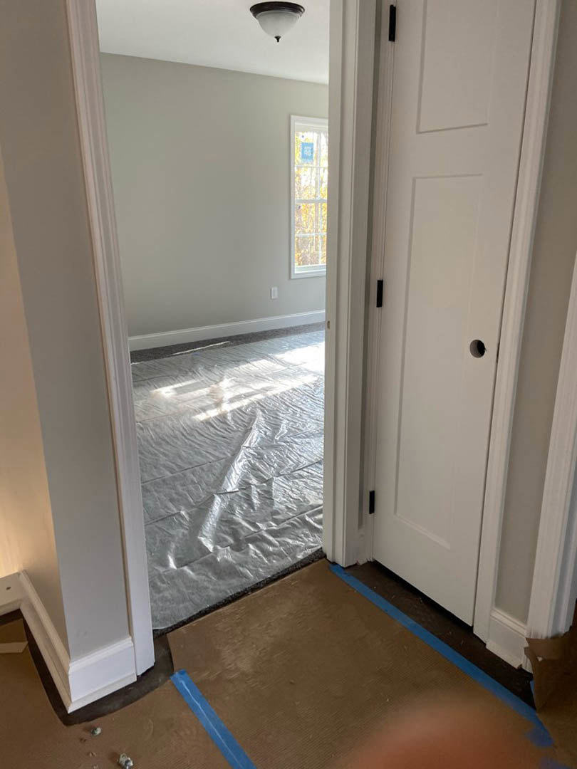 White door with a hole, plastic sheet covering the floor, white-framed window, close-up of lamp, unfinished walls in a remodeled room