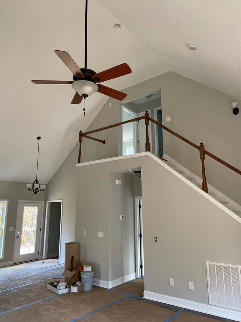 Ceiling fan with light fixture mounted on white plaster ceiling, white door with window, wall vent, black pole, and grey bucket with white label on floor
