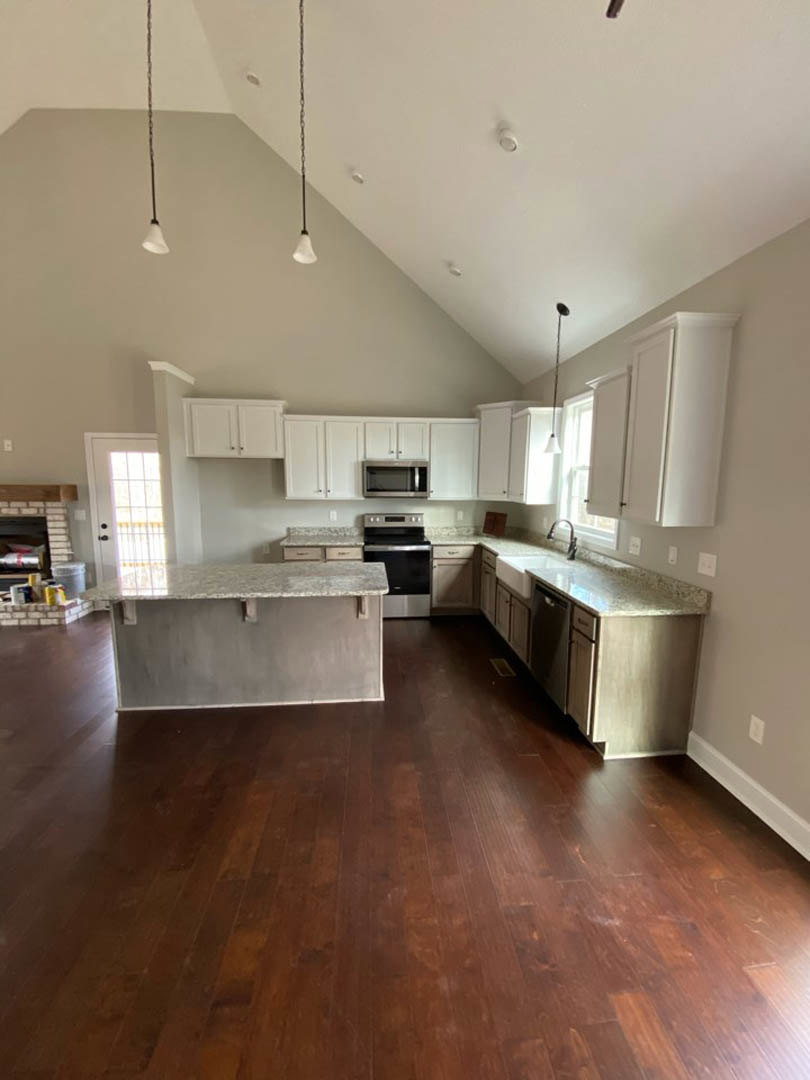 Kitchen with warm wood flooring, light-colored countertops, black oven, white cabinetry, stainless steel sink, and soft overhead lighting