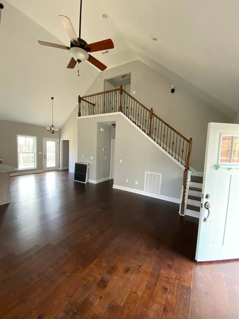 Hardwood floored room featuring a wooden staircase, white walls, ceiling fan with light fixture, and a paneled door.