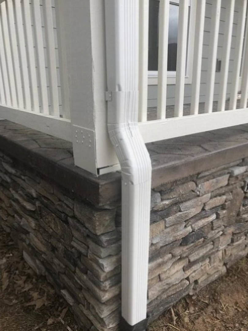 White composite handrail mounted on textured stone wall along outdoor porch stairs of residential home