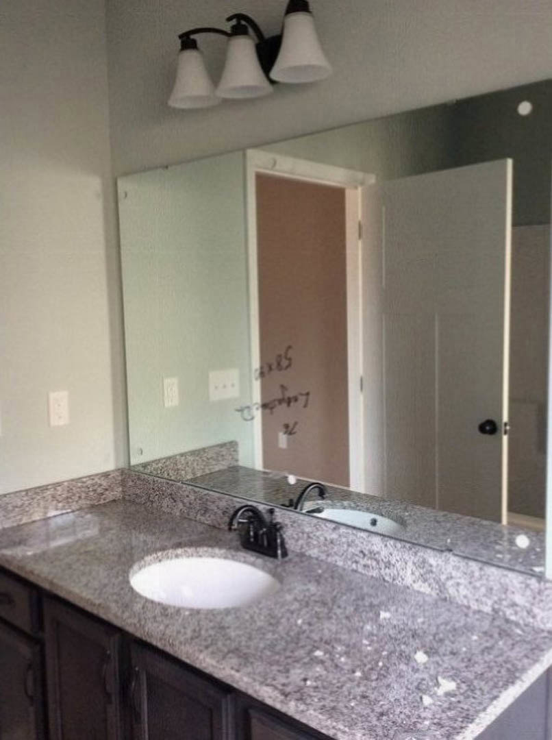 White quartz countertop with undermount sink, chrome faucet, large frameless mirror, white walls, black light fixture, and subtle grey tile backsplash