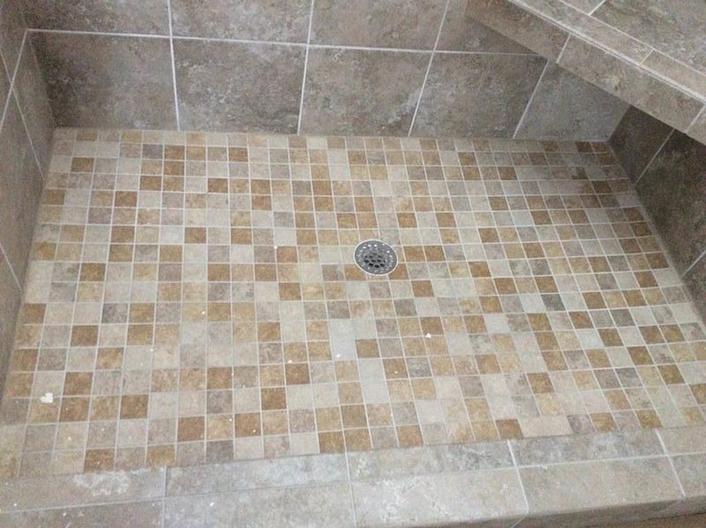 Grey tile shower floor with circular metal drain, surrounded by stone tile flooring
