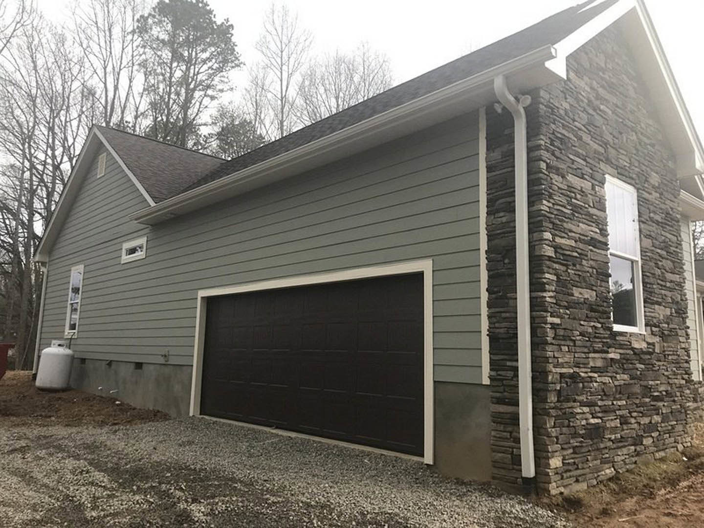 Two-story home with gray siding, white-trimmed windows, attached garage featuring a white paneled door, concrete driveway, and landscaped front yard with small trees.