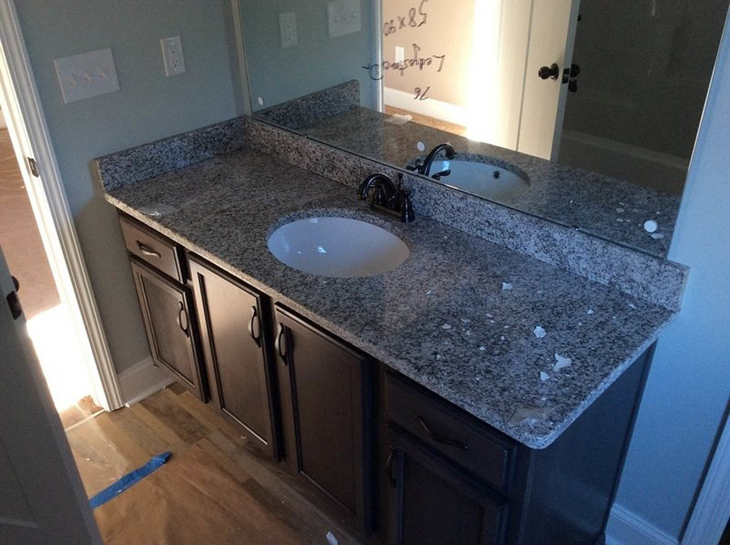 Bathroom with granite countertop, undermount sink, chrome faucet, large framed mirror, white tile backsplash, and white cabinetry