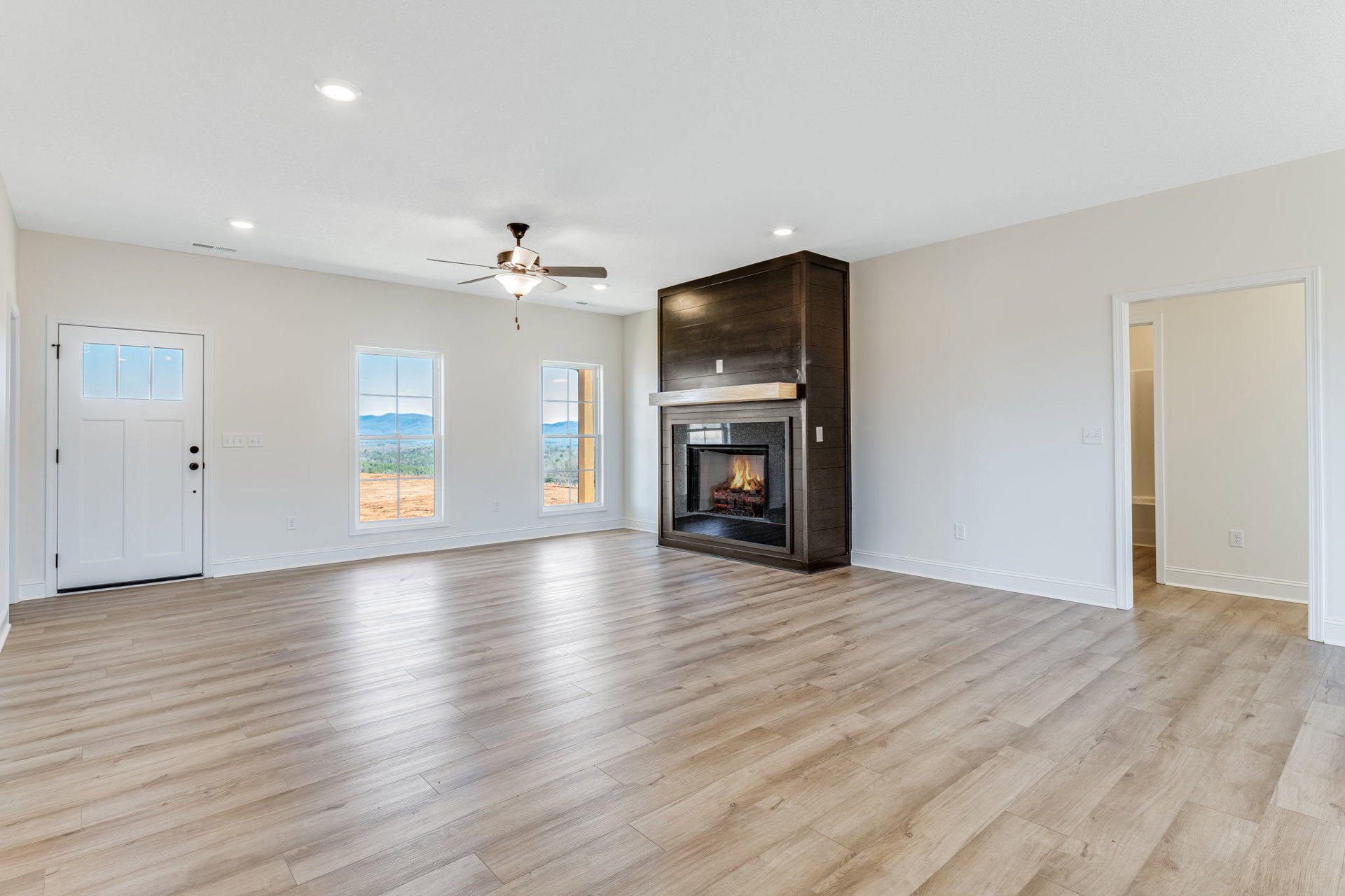 Living room with hardwood floors, wood mantel fireplace, ceiling fan with light, white door with glass panels, large window framing mountain view, plaster walls