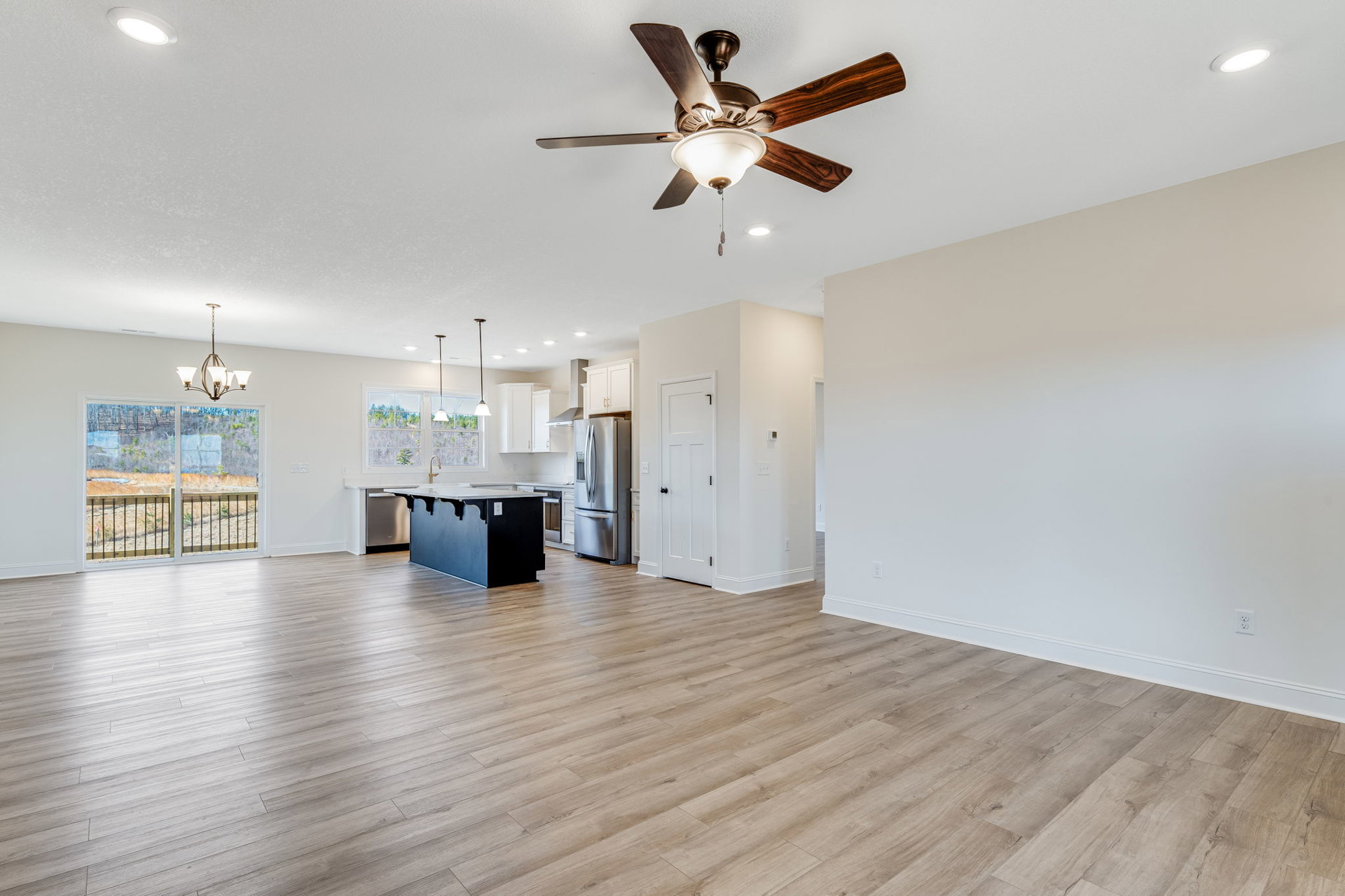 Open kitchen with black and white countertops, stainless steel refrigerator, wood laminate flooring, ceiling fan with light fixture, white door with black knob, sliding glass door