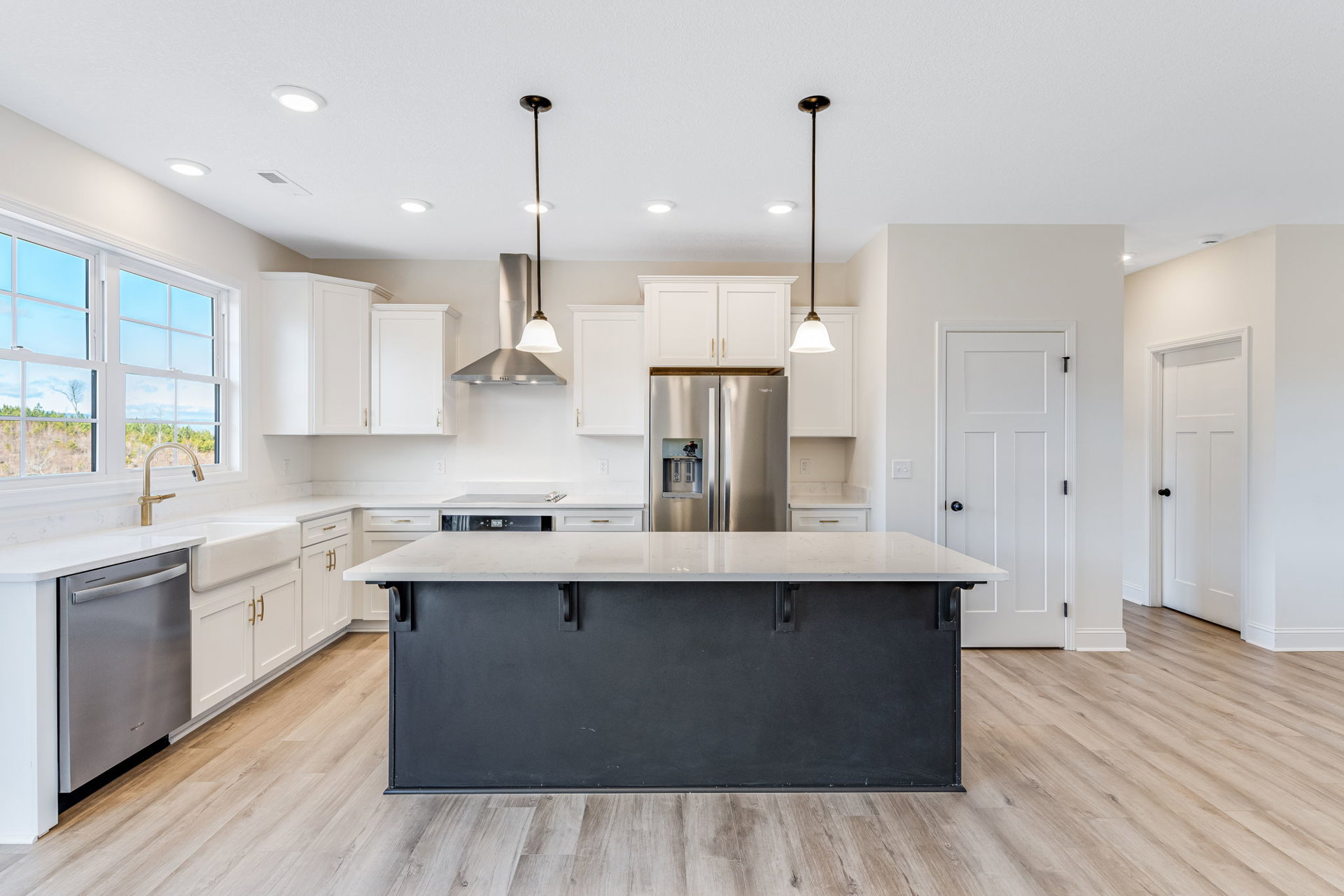 Spacious kitchen featuring a large white island countertop, stainless steel refrigerator with water dispenser, silver dishwasher, tile flooring, white cabinetry, and pendant