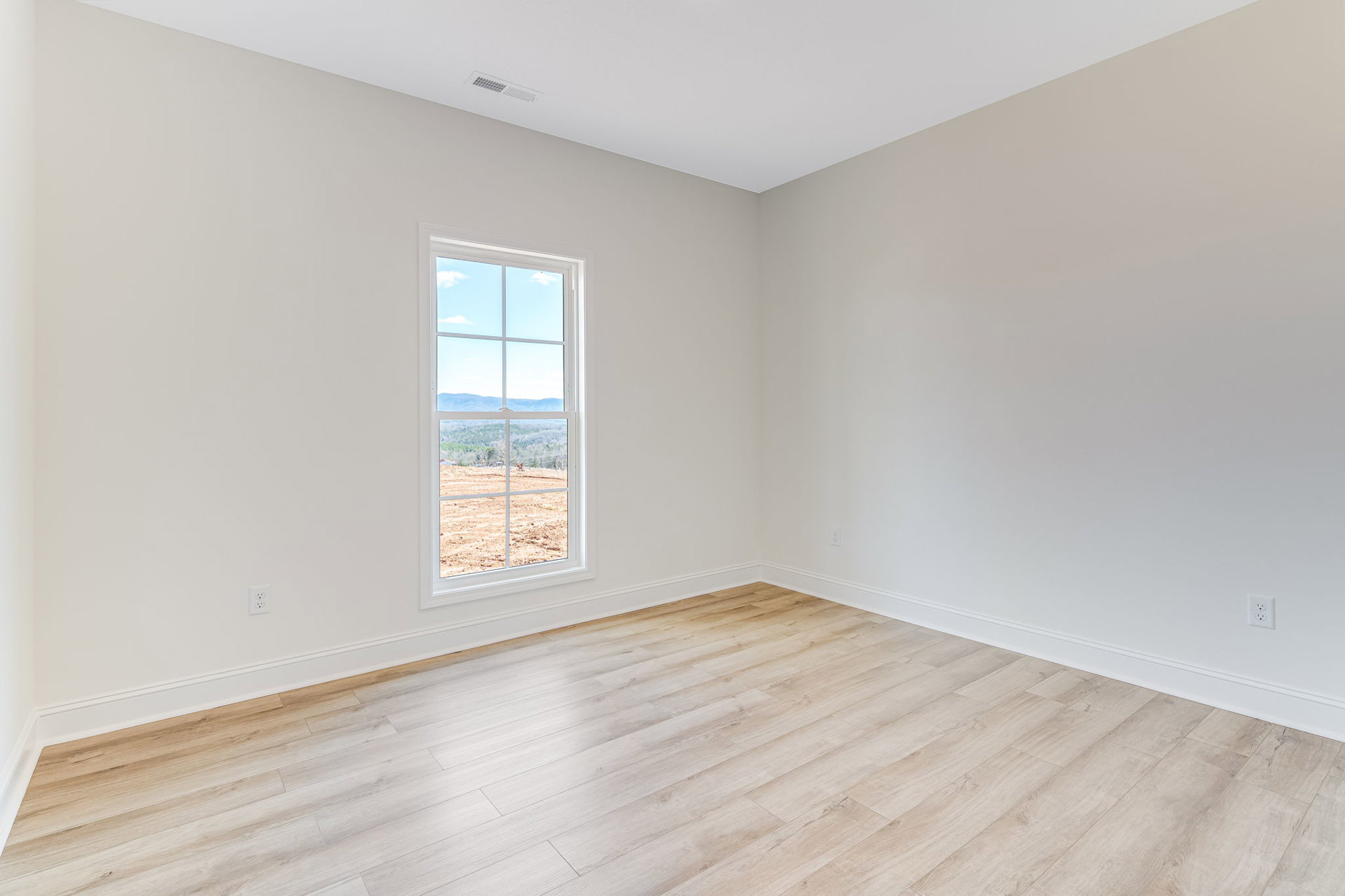 Hardwood floor and white ceiling in a bright room with a large window overlooking a field and distant mountains