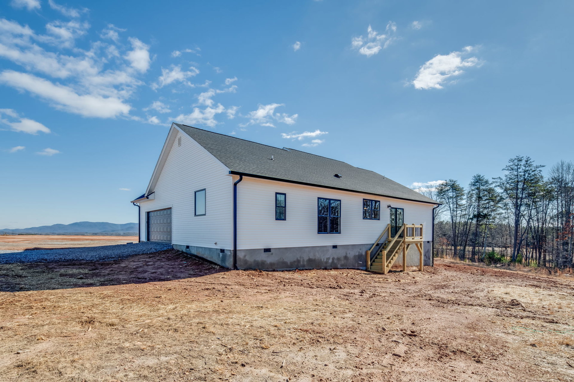Two-story house with attached garage, wooden exterior stairs, blue-framed window, fenced yard, dirt and grass landscaping, under partly cloudy sky
