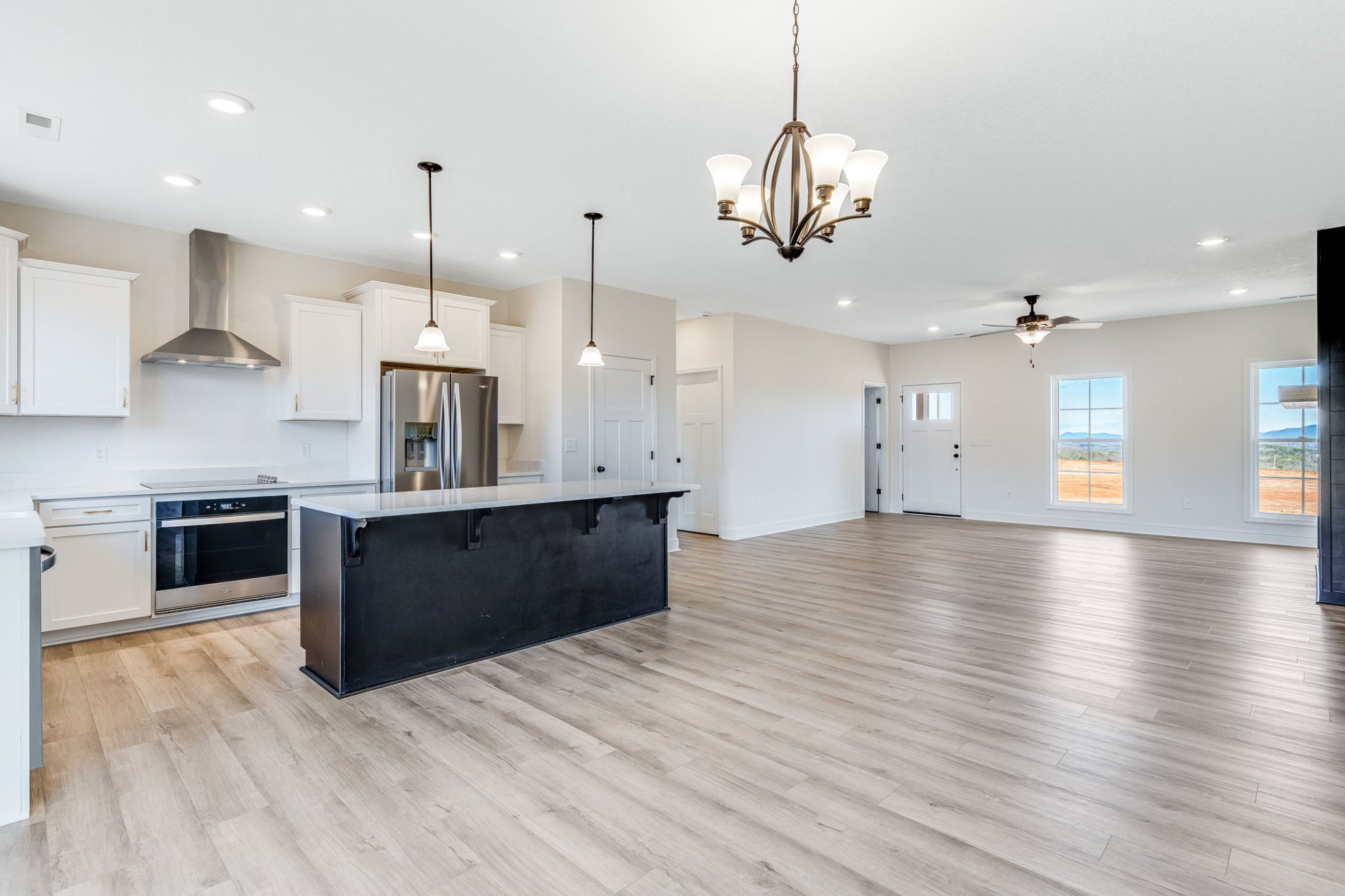 Open-concept kitchen and living room featuring a wood floor, black countertop island, stainless steel double-door refrigerator, black and silver microwave, large window overlooking