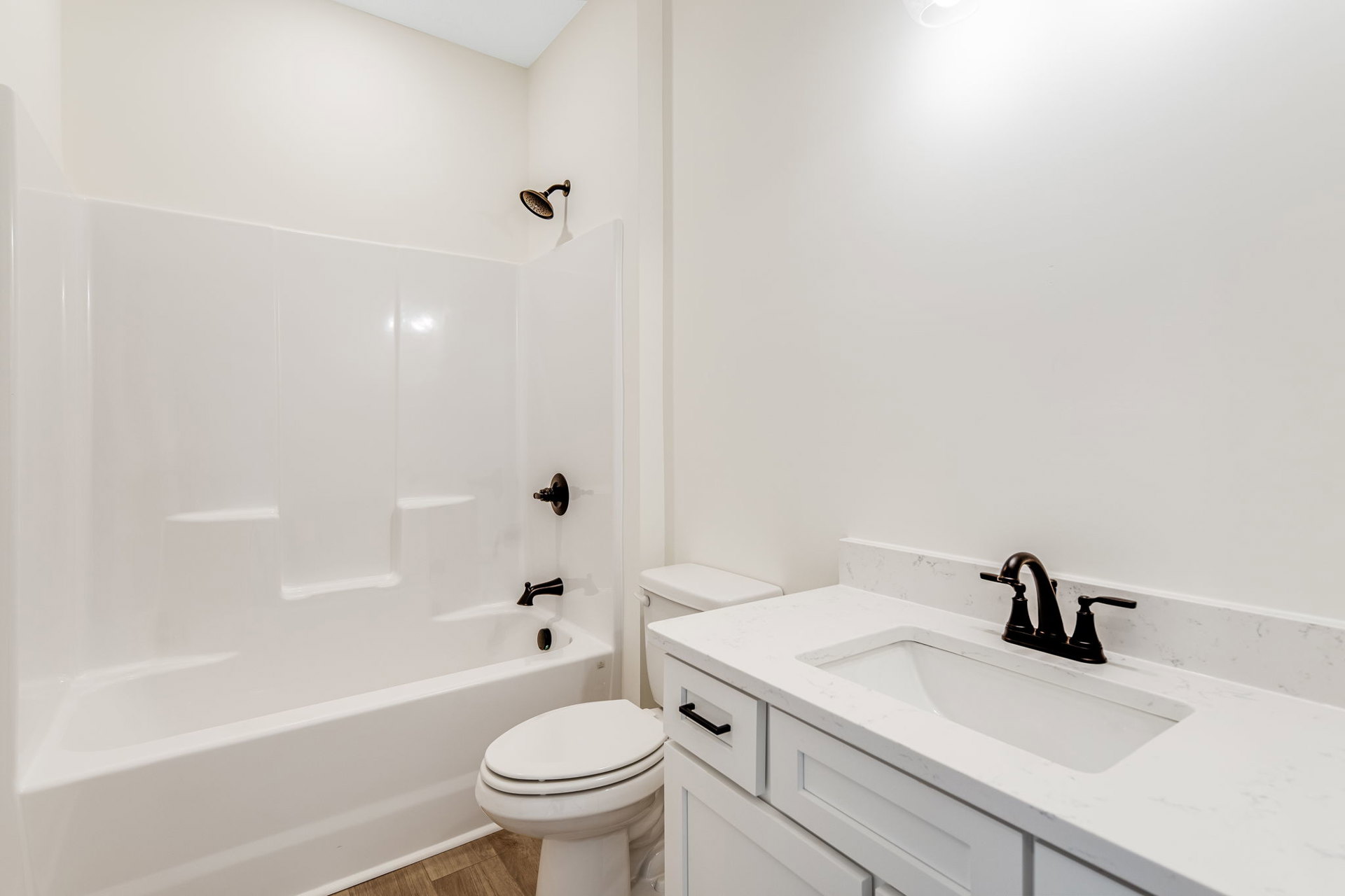 Bathroom with white sink featuring black faucet, white toilet with seat down, white bathtub, light tile walls, and chrome bathroom accessories
