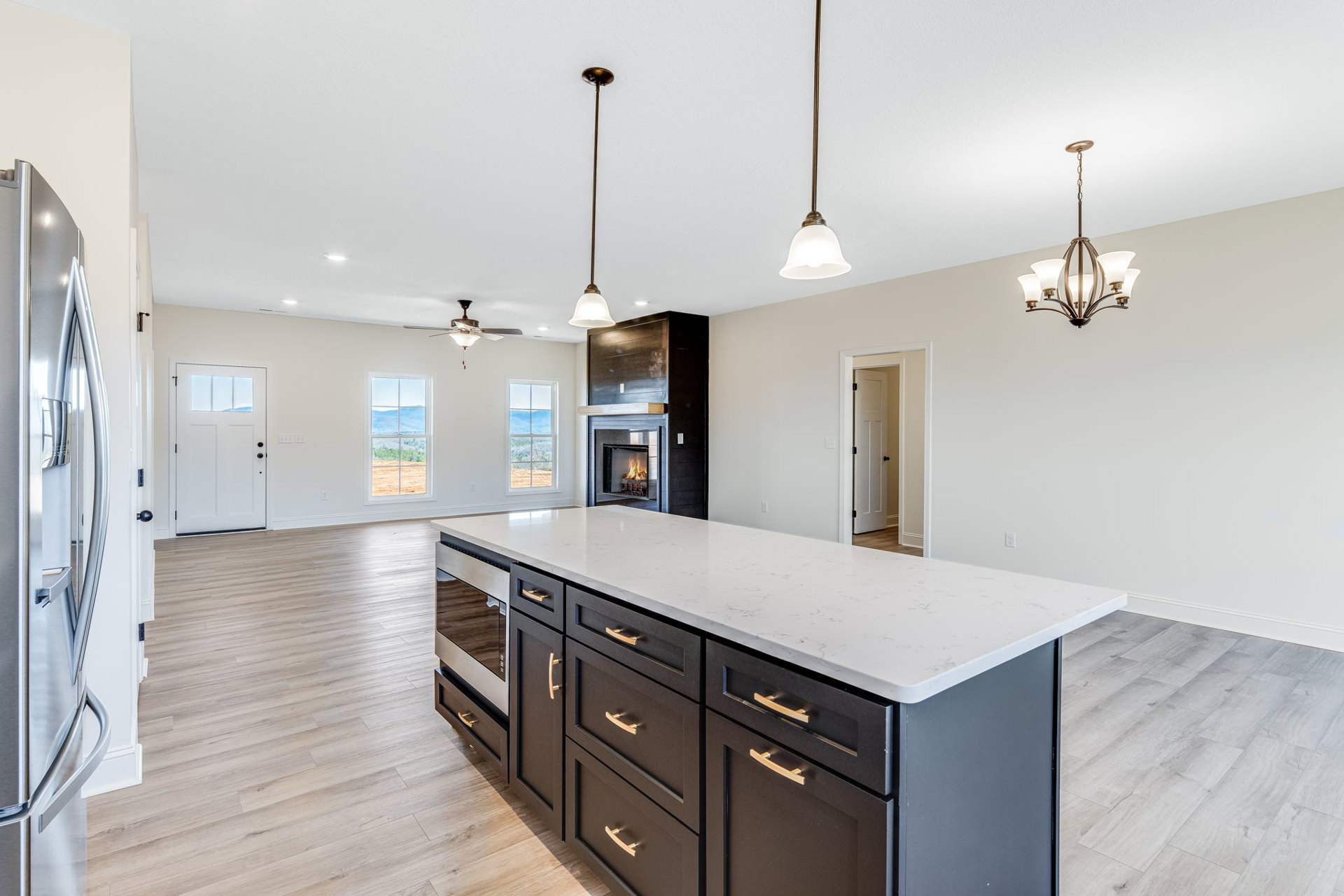 Kitchen with central fireplace, large island featuring drawers, white door with window, stainless refrigerator door handle, ornate chandelier, long metal pole with gold handle