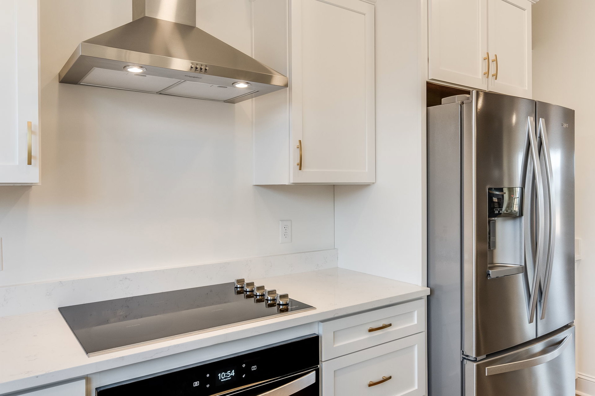 Stainless steel refrigerator and range, white cabinetry, quartz countertops, vent hood, and a window with white trim